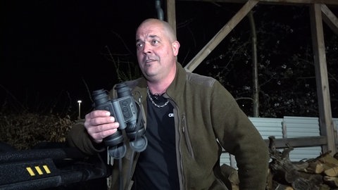 Dennis ist Jäger. Er trägt eine khakifarbene Jacke und hält ein Fernglas in der Hand.