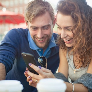 Ein Mann und eine Frau schauen lachend auf ein Handy | 10 Tipps fürs perfekte Online-Dating