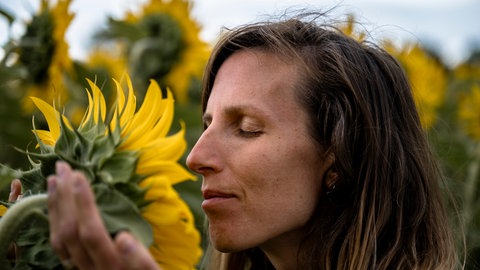 Person genießt den Geruch einer Blume. Der Geruchssinn kann durch positive oder negative Erlebnisse beeinflusst werden.