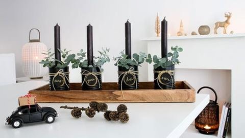 Etwas Grün, wie Moos oder Eucalyptus um die Kerzen herum stecken. Alle vier Dosen auf das Holztablett stellen und wer es gern üppiger mag, kann das Tablett mit zusätzlicher Dekoration bestücken.