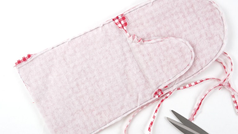 Die Innenseite aus Futterstoff rechts auf rechts auf die Außenseite aus Futterstoff legen, mit Stecknadeln fixieren und zusammensteppen. Die Nahtzugaben an den Rundungen auf 5 mm zurückschneiden, an der Unterkante jeweils 2 cm der Nahtzugabe stehen lassen