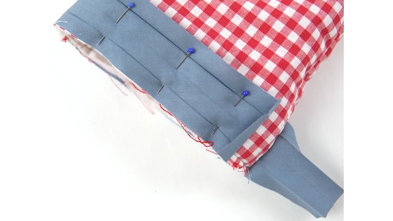 Die Eingriffkante mit Schrägband einfassen. Dazu den Handschuh auf links wenden. Das Schrägband der Länge nach aufklappen und rechts auf rechts an die Eingriffkante stecken, dabei das Schrägband am Nahtanfang 1 cm einklappen