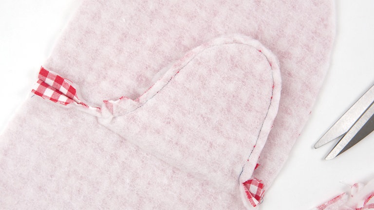 Ober- und Unterteil der Innenseite aus Futterstoff rechts auf rechts legen, mit Stecknadeln fixieren und entlang der Mittelnaht zusammensteppen. Die Nahtzugaben auf 5 mm zurückschneiden, an den Innenrundungen V-förmig einschneiden. An beiden Seiten 1,5 cm Nahzugabe stehen lassen. Die Mittelnaht an den Seiten auseinanderbügeln.