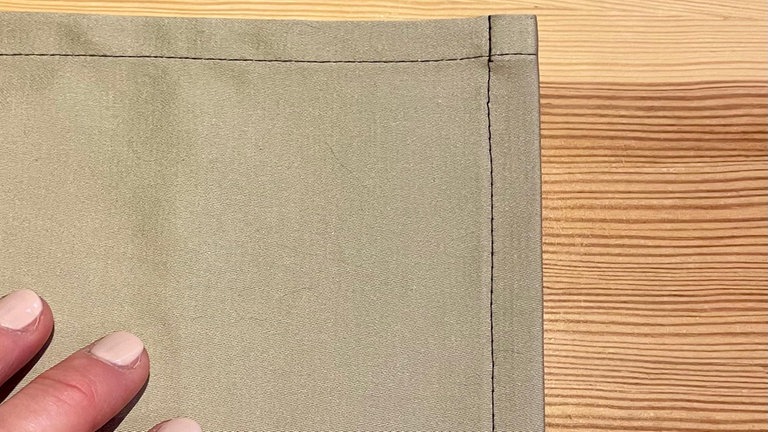 Zum Schluss noch den Saum der Schürze 2 cm nach innen umbügeln, Schnittkante einschlagen und schmalkantig festnähen (wie in Schritt 3).