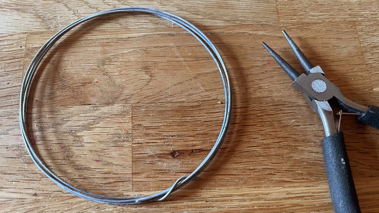 Das Drahtkränzchen abnehmen und die Drahtenden mit der Biegezange um das Kränzchen wickeln, sodass sie fixiert sind. Das Kränzchen von Hand vorsichtig zu einem Ei formen.