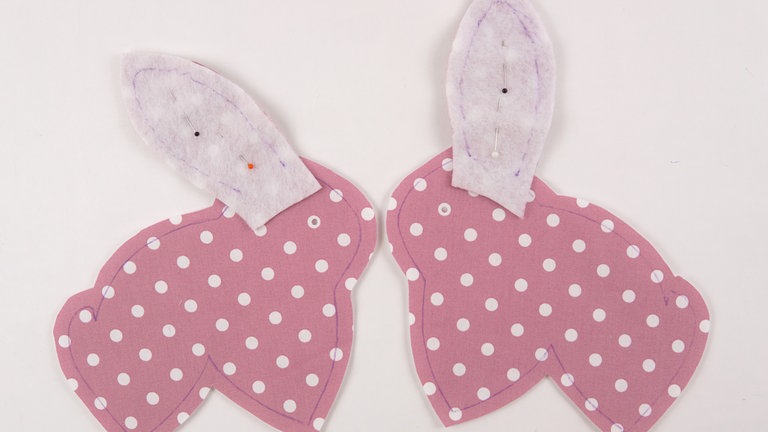 Die Ohren A+B  passgenau auf die Körperteile A+B stecken. Den Verlauf der Naht mit Hilfe der Schnittteile auf dem Volumenvlies anzeichnen. Alternativ können Sie die Schnittteile als Schablone aufheften und daran entlang nähen.