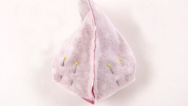 Die Stofflagen auseinanderziehen und an der unteren, noch offenen Kante so aufeinanderlegen, dass die beiden Nähte zusammentreffen. Die Bodennaht mit Stecknadeln fixieren.