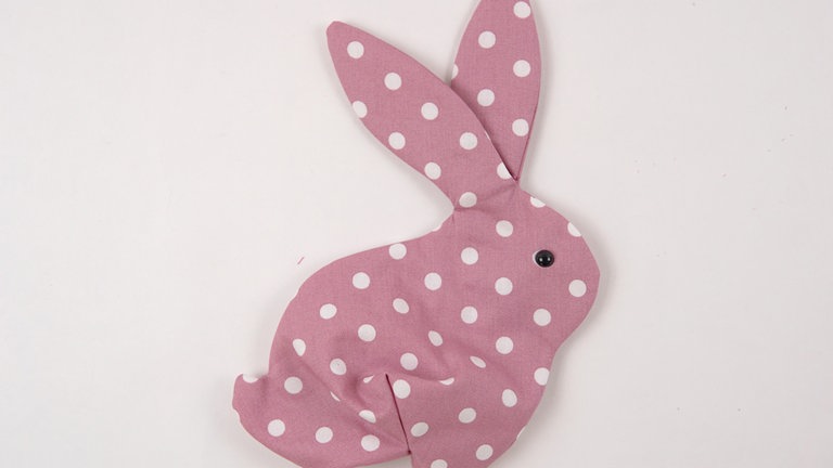 Das Osterhäschen durch die Wendeöffnung auf rechts wenden. Das Schwänzchen, den Kopf die Ohren und den Körper mithilfe eines kleinen Borstenpinsels oder einer Häkelnadel ausformen und die Augen nach Herstellerangabe anbringen.