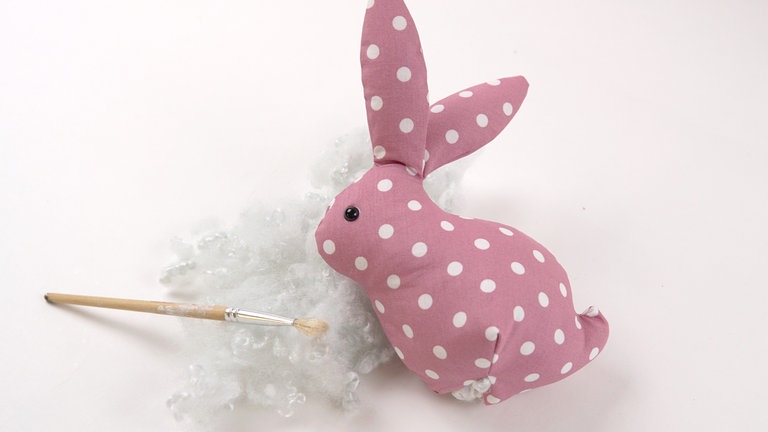 Zuerst die Ohren locker, dann den restlichen Körper fest mit Füllwatte ausstopfen. Für das Füllsäckchen entsprechend etwas Platz lassen.