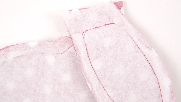 Die Naht schließen. Exakt an Nahtanfang und – ende der Ohren starten und enden. Darauf achten, dass kein anderer Stoff mit in die Naht gerät. Dafür vor dem Nähen die anderen Stofflagen etwas nach unten ziehen. Sie können die Naht auch leicht nach oben gerundet nähen.