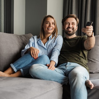 Paar sitzt auf der Couch und guckt TV