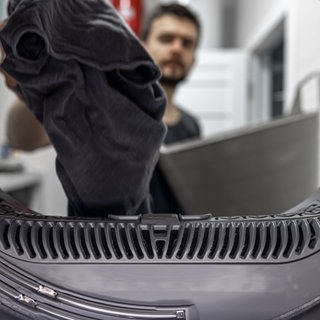 Sport- und Funktionskleidung richtig waschen - Mann vor Waschmaschine