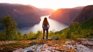 Frau steht auf einem Berg und schaut auf einen See
