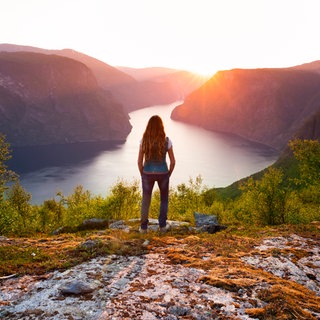 Frau steht auf einem Berg und schaut auf einen See
