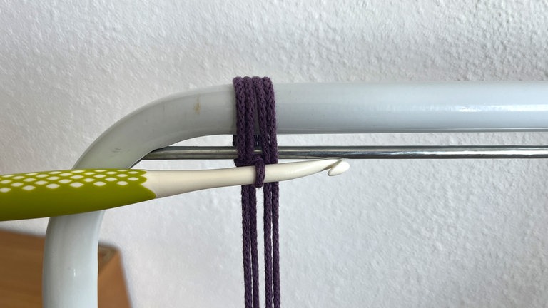 Die neu gebildete Schlaufe wird über die Häkelnadel gelegt und durch die erste hindurch gezogen, sodass wieder nur eine auf der Nadel liegt.