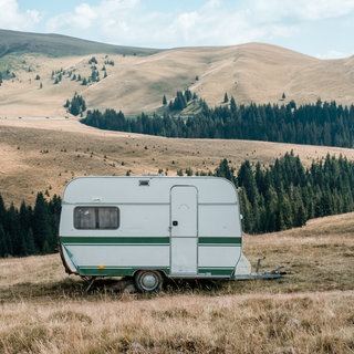 Ein kleiner Caravan mit dunkelgrünem Streifen steht inmitten einer Landschaft. 