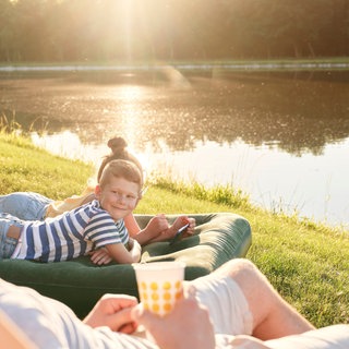 Zwei Kinder liegen auf einer Luftmatratze, ein Mann schaut zu den Kindern. Welche Campingluftmatratze die Nacht im Zelt gemütlich macht, wie schnell das Aufpumpen klappt und ob Schadstoffe drin sind: Wir checken sechs Luftmatratzen. 