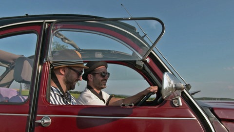 Zwei lachende Männer fahren in einer Ente