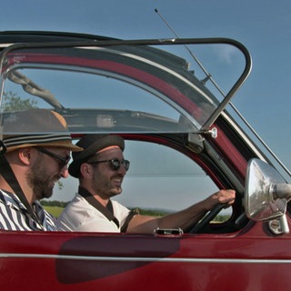 Zwei lachende Männer fahren in einer Ente