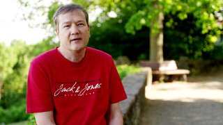 Eric Hass sitzt auf einer Mauer.