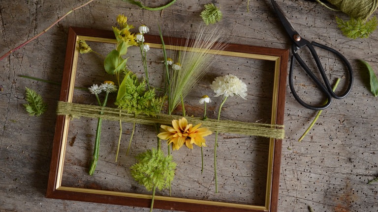 Darauf achten, dass die eher instabilen Blumen alle gemeinsam in eine Richtung stecken, sodass man den Rahmen so hängen. 