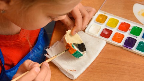 Ein Mädchen bemalt ein Schälchen aus Salzteig: Der Teig – herzustellen nach unserem Rezept – lässt sich wie Modelliermasse bearbeiten, trocknen und bemalen.