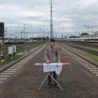 Mann mit Bügelbrett am Bahnhof