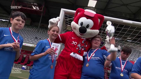 Junge Fußballer mit Medaillen und Pokal posieren mit einem Maskottchen