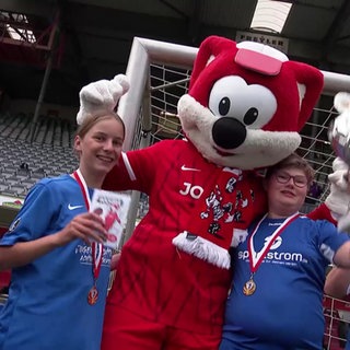 Junge Fußballer mit Medaillen und Pokal posieren mit einem Maskottchen