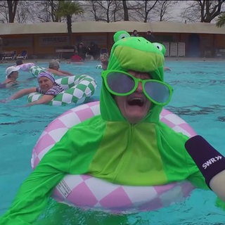 Eine verkleidete Frau wird im Schwimmbecken in einem Schwimmring interviewt