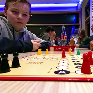 Ein Junge sitzt bei einem Turnier an einem Mensch-ärgere-dich-nicht-Spielbrett