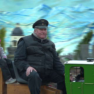 Kinder und Erwachsene fahren auf einer kleinen Lok durch eine Miniaturlandschaft auf dem Stuttgarter Weihnachtsmarkt