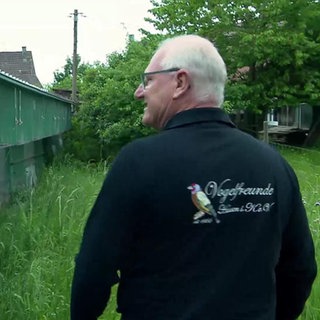 Vogelzüchter Wolfgang Stauß läuft in einem Garten mit Vogelkäfigen