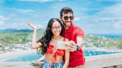 Ein Pärchen auf einer Aussichtsplattform im Urlaub macht ein Selfie | Digitale Urlaubsgrüße: Mit diesen Apps könnt ihr digitale Postkarten verschicken