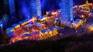 Wundervolles Winterwissen - der SWR1 Adventskalender: Woher kommt der Weihnachtsmarkt. Das Bild zeigt den Weihnachtsmarkt in der Ravennaschlucht. Die Höllentalbahn fährt über das blau beleuchtete Viadukt über der Ravennaschlucht, während darunter der Weihnachtsmarkt stattfindet.