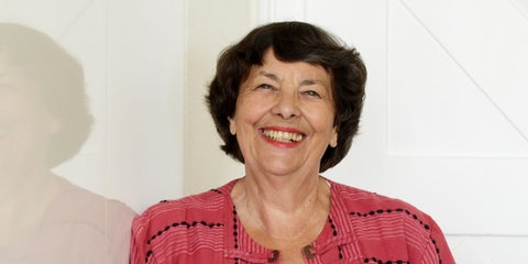 5 Tipps vom Profi: so feiern Sie ruhige und entspannte Weihnachten mit der Familie. (Portrait-Aufnahme von Business-Coach Ursula Kraemer aus Friedrichshafen - die dunkelhaarige Frau lächelt in die Kamera, trägt ein dunkel-rosé-farbenes, leichtes Jackett mit Knopf-Applikationen über einem weißen T-Shirt und steht vor einem Hintergrund aus weiß lackiertem Holz)