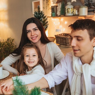 Eine junge Familie sitzt gemütlich und zufriedend lächelnd an einem Tisch inmitten von Weihnachtsdekoration