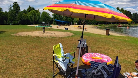 Am Blausee im Rhein-Neckar-Kreis liegt eine Frau entspannt auf einem Handtuch unter einem Sonnenschirm. Der See ist das ideale Ausflugsziel für einen Urlaub in Baden-Württemberg.