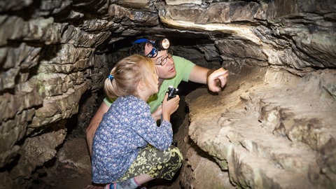 Ein Mann und eine Frau kauern mit Stirnlampen in der Sieben-Täler-Höhle. Die Sieben Täler Runde bei Rottenburg gehört zu den schönsten Wanderwegen in Baden-Württemberg.
