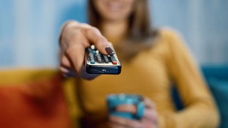 Frau sitzt auf der Couch mit Tee und Fernbedienung in der Hand