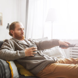 Mann sitzt auf der Couch mit der Fernbedienung in der Hand
