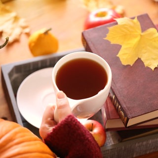 Frau hält Tasse mit Tee und Bücherliegen auf dem Tisch