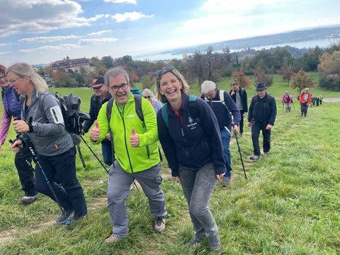 SWR4 Moderator Holger Bentzien geht in einer grünen SWR4 Jacke mit einer Wandergruppe einen Berg am Bodensee hinauf, schaut in die Kamera und hält beide Daumen nach oben.