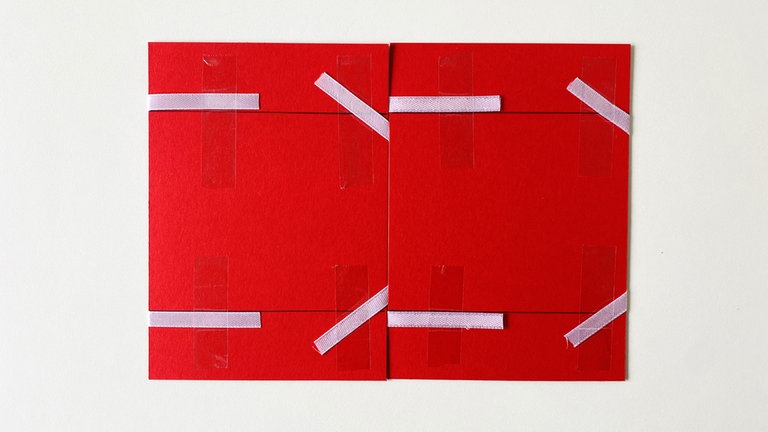 Jetzt werden die rechten Enden der Bänder nach innen umgeklappt und mit einem Klebestreifen fixiert. Das obere Band zeigt dabei nach oben, das untere nach unten.