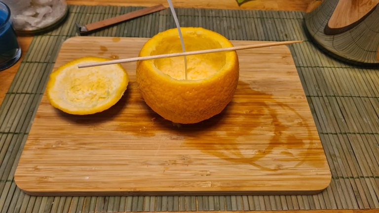 Der Docht wird mittig in die ausgehöhlte Halb-Orange gesetzt und anschließend mit den Holzstäbchen fixiert, sodass er gerade stehen bleibt und nicht verrutscht oder umkippt