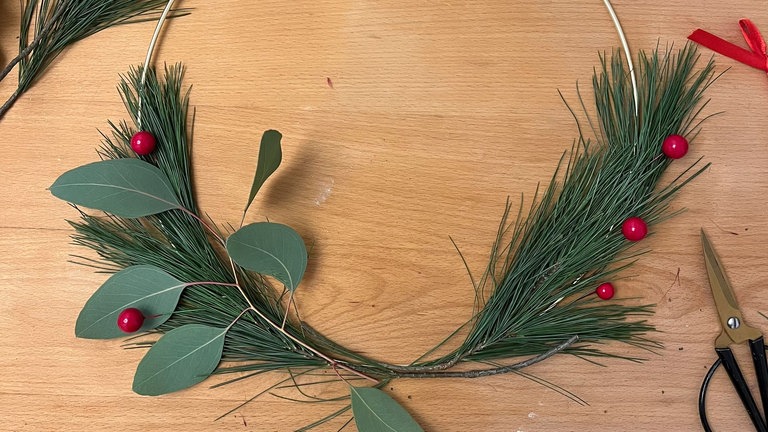 Danach ein Eukalyptusbündel leicht versetzt auflegen – wieder mit Draht fixieren. Schrittweise weiterarbeiten, bis ein gleichmäßiger Verlauf entsteht.