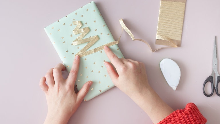 Jetzt das Band hin und her legen: Oben starten mit einem sehr kurzen Abschnitt, dann das Band nach links legen und nach unten ein kleines Stück ziehen. Wieder zurück nach rechts legen und ein Stück länger ziehen.
