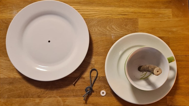 Anschließend das robuste Garn zu einer Schlaufe zusammen führen. Diese wird unter eine Unterlegscheibe gelegt, die Schraube durch den Knoten und anschließend durch das Loch im großen Teller stecken