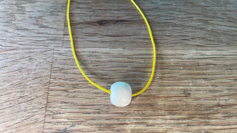 1,5 m von der Nylonkordel abschneiden. Eine Holzperle auffädeln und beide Fadenenden auf die gleiche Länge ziehen.