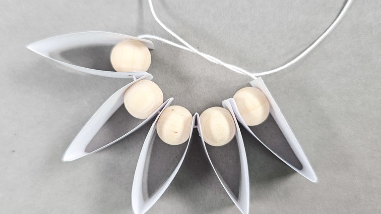 Den Faden so eng es geht anziehen, darauf achten, dass der Anfang und das Ende des Papierstreifens innen aufeinanderstoßen und die Schnur verknoten.